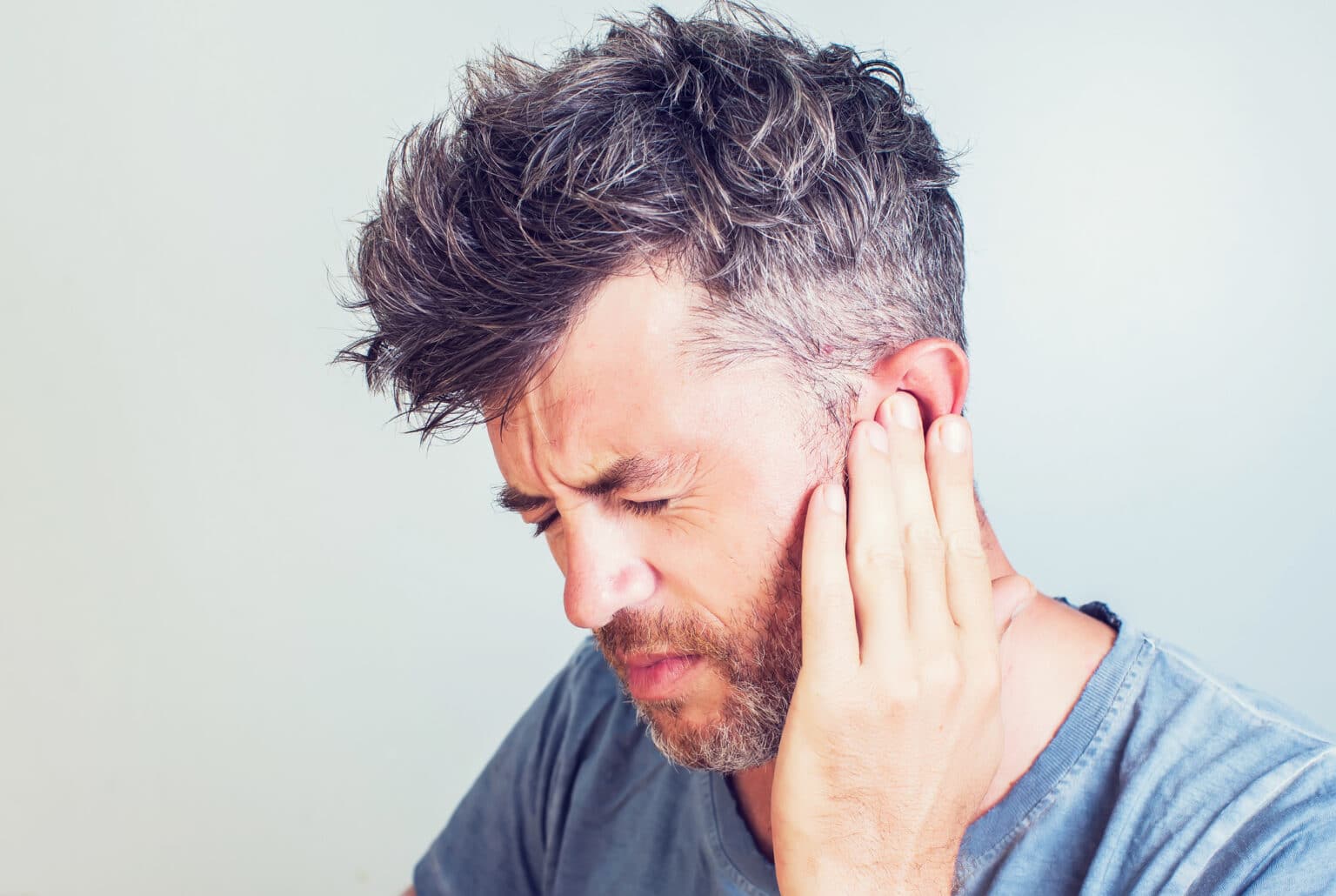 Man with tinnitus pressing his ear with his hand.