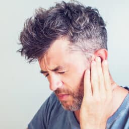 Man with tinnitus pressing his ear with his hand.