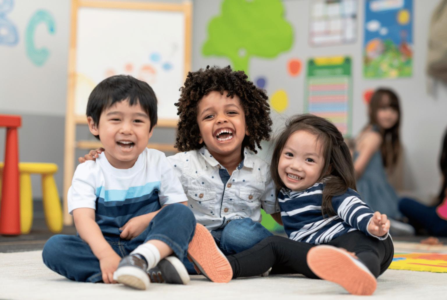 three toddlers smile in a brightly colored classroom