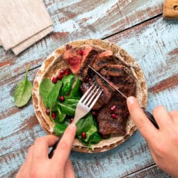 Man eating a steak and spinach on a wooden table.