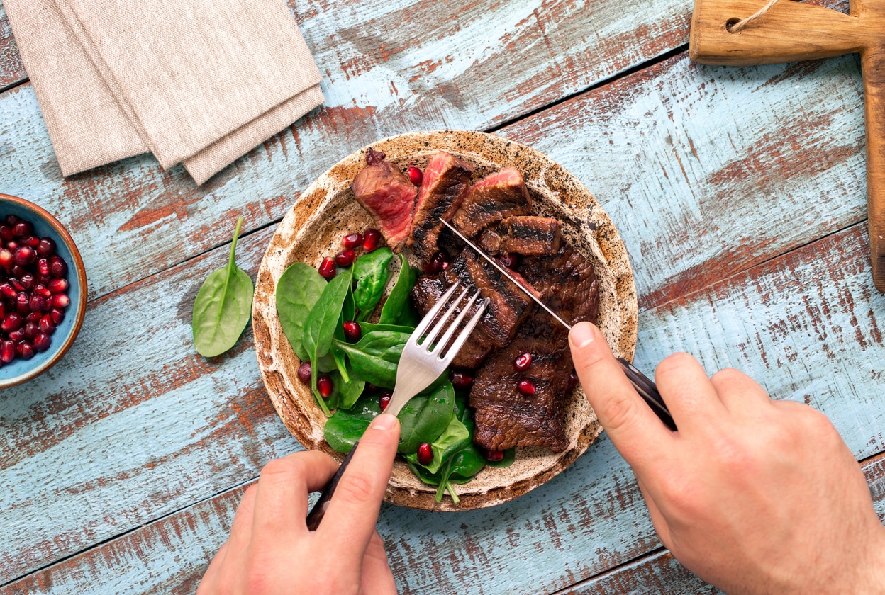 Man eating a steak and spinach on a wooden table.