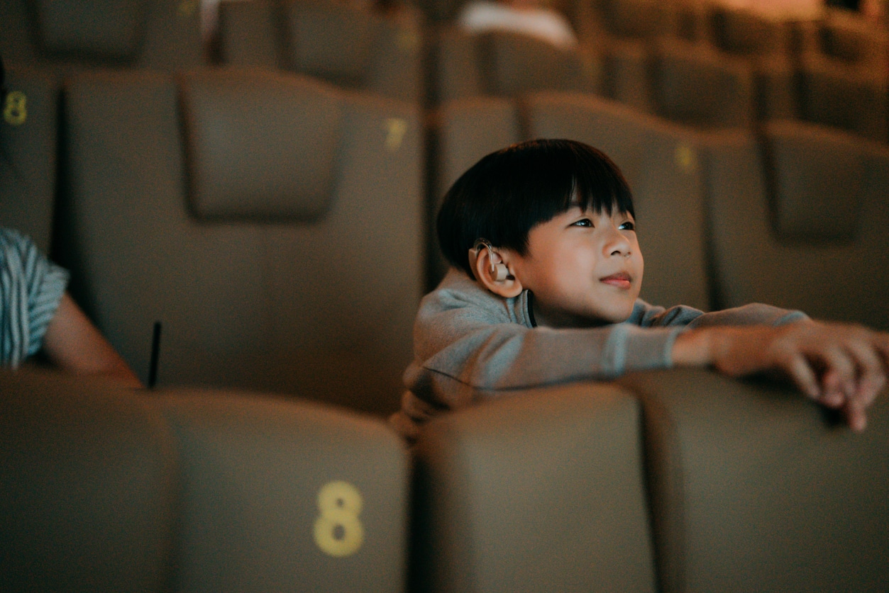 Young boy with hearing aids smiling in a theater.