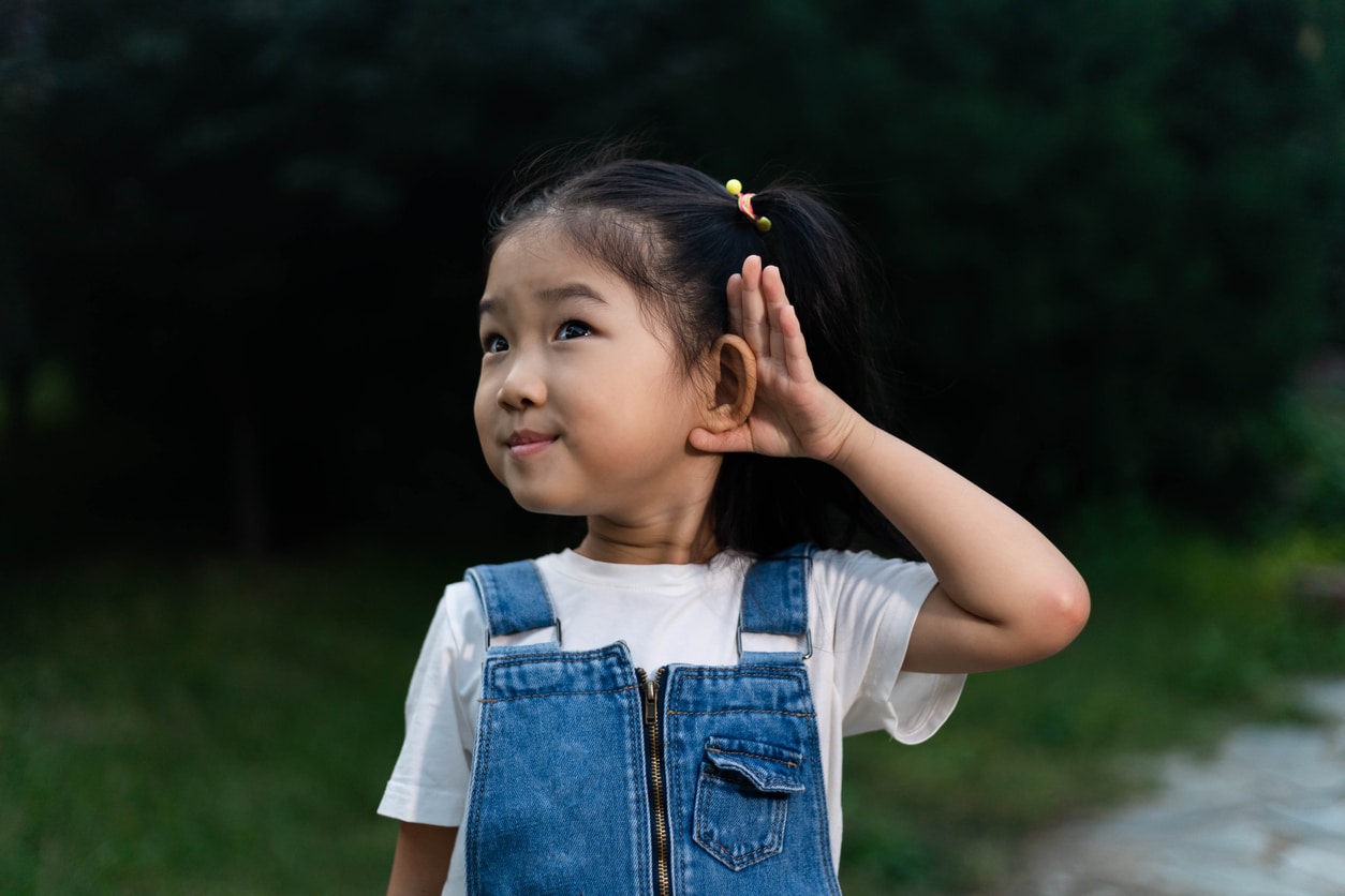 Young girl holds hands behind ear outside 
